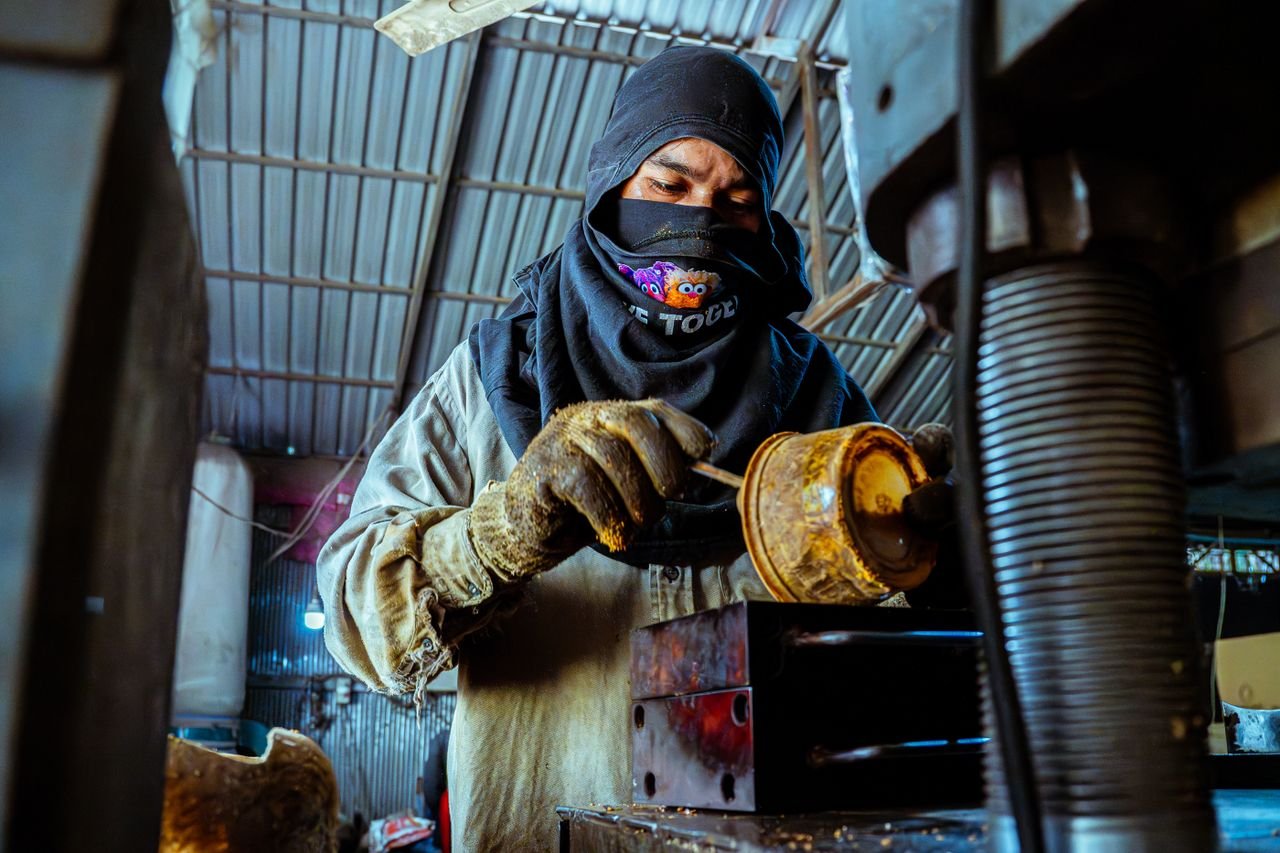 A masked industrial worker operates machinery in a factory setting, highlights labor and craftsmanship.